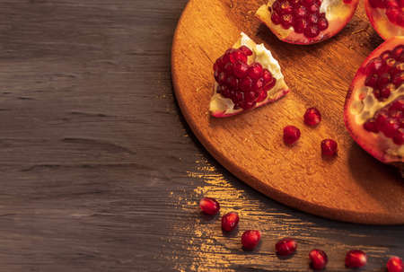 The juicy pomegranate, cut into uneven parts, lies on a round boardの写真素材