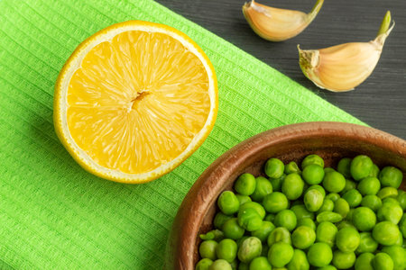The horizontal photo shows an image of a green pea and half a lemon. The peas are in a shallow...