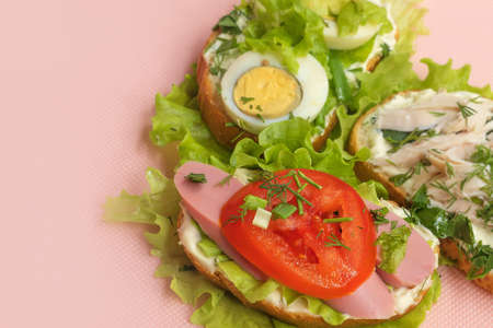 Three homemade sandwiches with egg, sausage, chicken and parsley lie on a pink backgroundの写真素材
