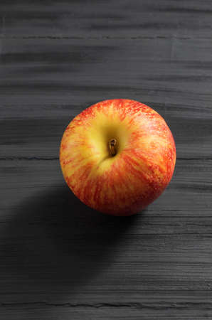 The vertical photo shows an image of a ripe fruit. This is a small apple. The apple is whole, with a rind and round, mostly red in colorの写真素材