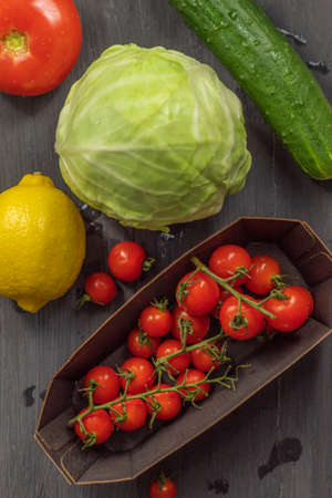 The vertical orientation of the photo shows the image of fresh, raw and healthy food. Here are vegetables such as white cabbage, carrots with earth elements, cucumber, cherry tomatoes, as well as one lemonの写真素材