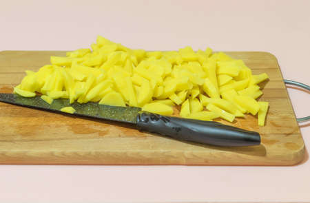 A photo with a pink background shows food. These are raw potatoes, cut into small pieces. The food is on a rectangular board with a knifeの写真素材
