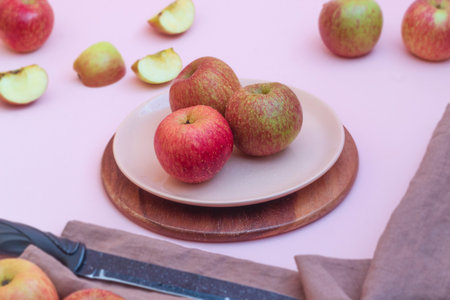 The photo shows an image of fresh fruit. These are whole and raw apples that lie on a plate and near...