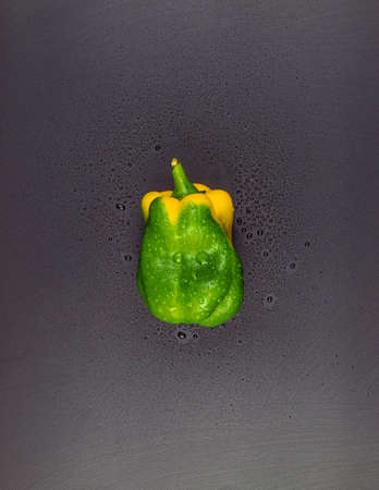 On a black background, from the upper angle, there is an image of fresh homemade vegetables. Here is a sweet pepper, whole, with drops of water on the peelの写真素材