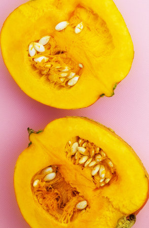 Two fresh pumpkin halves lie on a pink backgroundの写真素材