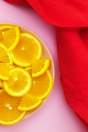 Juicy orange slices lie in a plate on a pink background with a red kitchen towelの写真素材