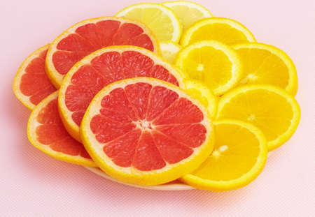 On a pink background in a ceramic plate are fresh slices of lemon, orange and grapefruitの写真素材