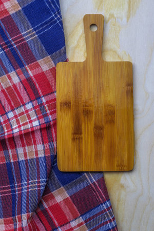 A checkered kitchen towel and a bamboo board lie on a wooden table