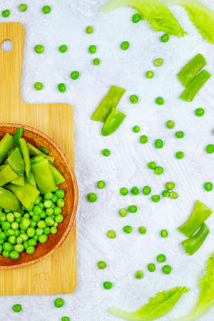 In the vertical photo, green beans and peas in fresh frozen form lie in a bamboo plateの写真素材