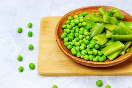 Green beans and green peas are lying on a bamboo board in a wooden bowlの写真素材