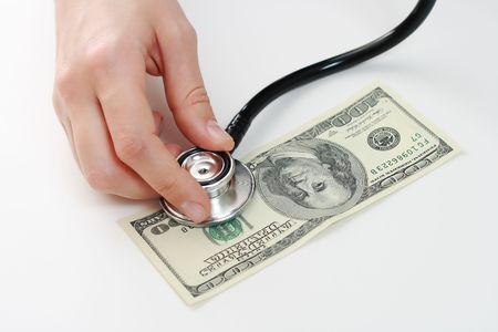 Doctor holding stethoscope in her fingers against one hundred u.s. banknote at the white tableの写真素材