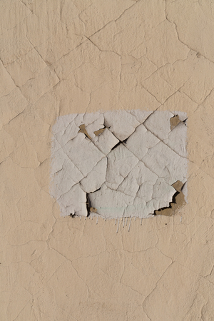 Skin paint on the wall of the building. Cracks on the surface. White rectangle on a beige wall.の写真素材