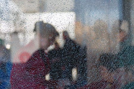 Blurred silhouettes of people behind broken glass. Fine mesh of cracks. Creative background. Female profile. Bus stop. Broken hopes. Diffused light.の写真素材