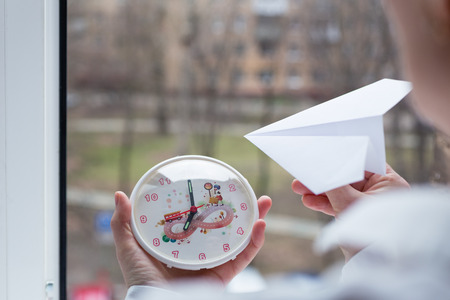 The girl is holding a watch and a paper airplane. Action to launch aircraft in support of the Telegram application. A popular messenger Telegram is banned in Russia.の写真素材