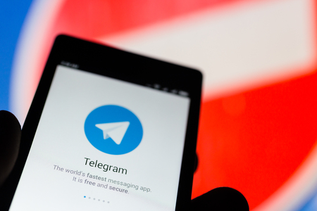 MOSCOW, RUSSIA - APRIL 17, 2018: A mobile phone in the hand with the Telegram application on the background of prohibiting sign. A popular messenger Telegram is banned in Russiaのeditorial素材