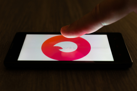 MOSCOW, RUSSIA - August 19, 2018: A smartphone lying on a table in the dark, displaying the logo of the Tinder app. The finger above touch screen. The concept of internet hookup dating dependence.のeditorial素材