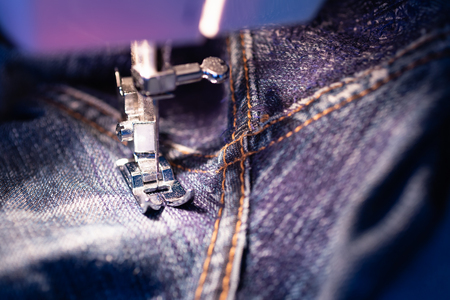 Repair jeans on the sewing machine. View of the fabric, needle and thread. Illumination from the built-in incandescent lamp. Jeans are a type of trousers, typically made from denim or dungaree clothの写真素材