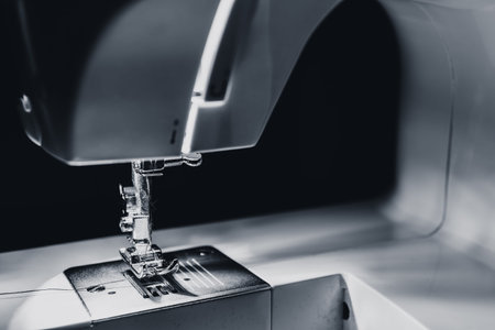 Modern compact electric sewing machine in the evening. View of needle and thread. Illumination from...