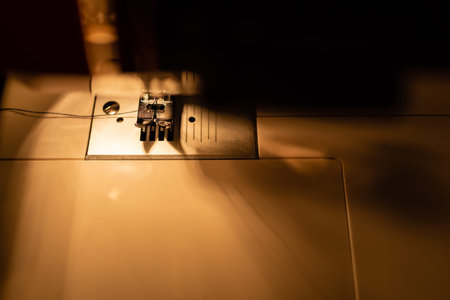 Modern compact electric sewing machine in the evening. View of needle and thread. Illumination from...