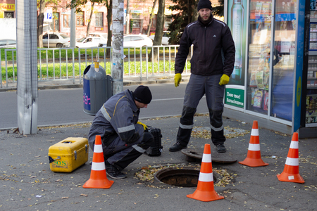 DNIPRO, UKRAINE - NOVEMBER 1, 2018: Employees of a telephone company near an open underground hatch repairing a communication line. Two guys in uniform with orange cones fencing troubleshootのeditorial素材