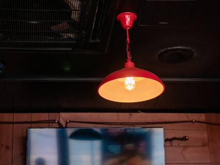 Lamp with a red lampshade under a dark ceiling. LED filament bulb. Photo through the glass of a cafe. Wood panels on the walls.の写真素材