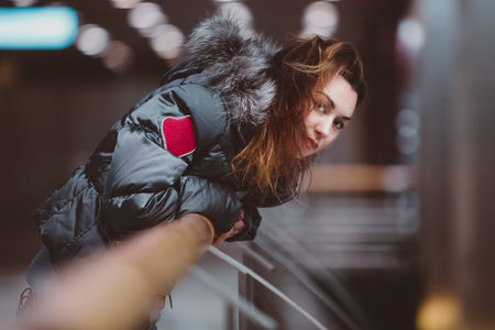 Young woman leans on railing. Girl with long hair in jacket looks from side. A brunette in...