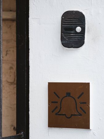 The intercom on the white wall of the house and the emblem with a bell icon. Intercom with a call button and a plate with a bell picture. Call communication device to enter into apartment building.の写真素材