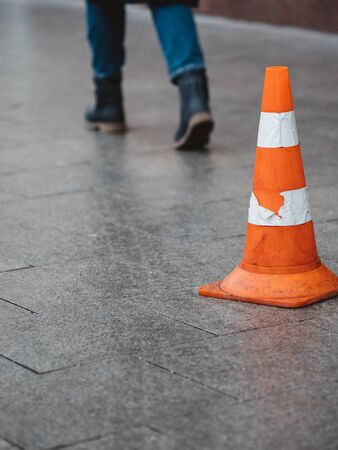 Orange plastic safety cone with strips of retro reflective film on the sidewalk paved with granite tiles in Moscow, Russia. Walking people legsの写真素材