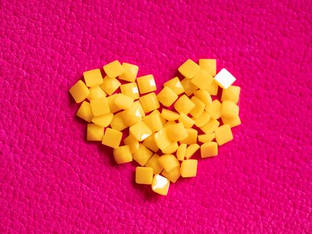 Yellow crystal craft handmade heart shape for diamond embroidery hobby rhinestone. Background with bright leather texture. Pink piece of natural tanned calfskin painted and treated. Macro lens shotの写真素材
