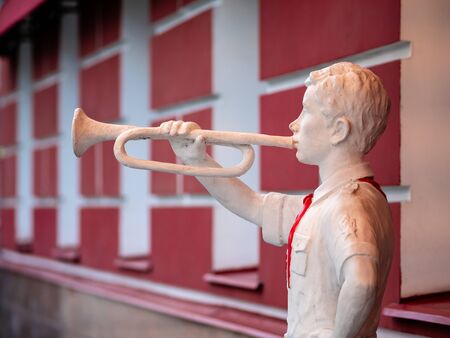 The figure of a pioneer with clarion in his hand near building. White sculpture of a boy with a red tie from the time of the Soviet Union era. Vintage silhouette of white plaster in Moscow, Russiaの写真素材