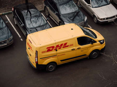 Moscow, Russia - March 11, 2020: DHL Deutsche Post courier in yellow-red uniform near minivan with company logos. DHL International GmbH is world largest courier, parcel, and express mail serviceのeditorial素材