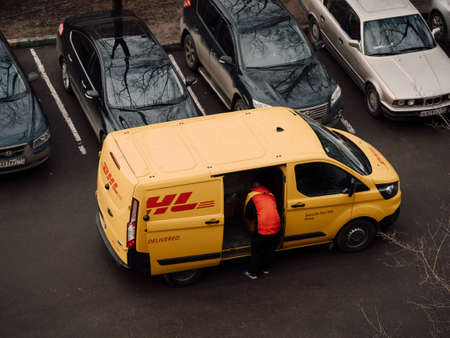 Moscow, Russia - March 11, 2020: DHL Deutsche Post courier in yellow-red uniform near minivan with company logos. DHL International GmbH is world largest courier, parcel, and express mail serviceのeditorial素材