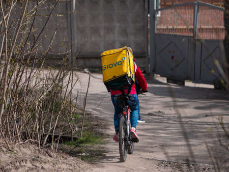 Dnipro, Ukraine - March 27, 2020: GLOVO delivery woman courier on bike with branded yellow thermal backpacks deliver customer orders. City has been quarantined due to threat of coronavirus pneumoniaのeditorial素材