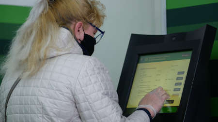 Dnipro, Ukraine - March 27, 2020: Woman in black protective mask and disposable gloves at Privatbank ATM. City has been quarantined. Due to threat of spread of coronavirus emergency state is declaredのeditorial素材