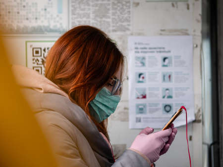 Dnipro, Ukraine - March 27, 2020: Lady in medical mask and gloves rides in trolley bus. Safety leaflet from COVID-19 in background. Due to threat of spread of coronavirus emergency state is declaredのeditorial素材