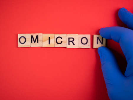Omicron variant replaces Delta. Emergence of new dangerous strain of coronavirus COVID-19 Omicron. Blue gloves on hand. Words omicron on colored red backgroundの写真素材