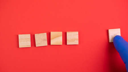 Hand in blue gloves point on clean wooden blocks on colored red background. Medical scientific or biological theme. Template for text or concept. Advertising mock up. Presentation flat lay mock upの写真素材