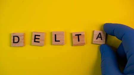 Omicron variant replaces Delta. Emergence of new dangerous strain of coronavirus COVID-19 Omicron. Blue gloves on hand. Word Delta on colored yellow backgroundの写真素材