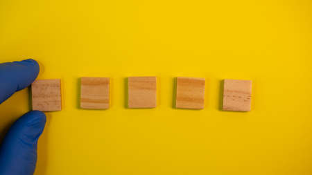 Hand in blue gloves point on clean wooden blocks on colored yellow background. Medical scientific or biological theme. Template for text or concept. Advertising mock up. Presentation flat lay mock upの写真素材