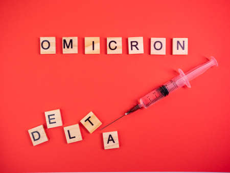 Omicron variant replaces Delta. Emergence of new dangerous strain of coronavirus COVID-19 Omicron. Syringe. Words omicron delta on colored red backgroundの写真素材