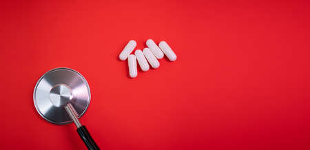 White drug capsules on colored red paper texture background. Macro close up pill medication. Big pharma. Off label approved medicine drugs use. Pharmacy concept. Copy space. Mock up design template.の写真素材