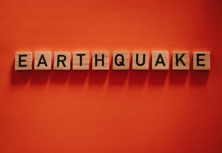 Inscription earthquake from vibration moves on background. Concept of earthquake, destruction and shifts of  earth's crust. Wooden square blocks with letters are laid out on  orange sheet. Slow motionの写真素材