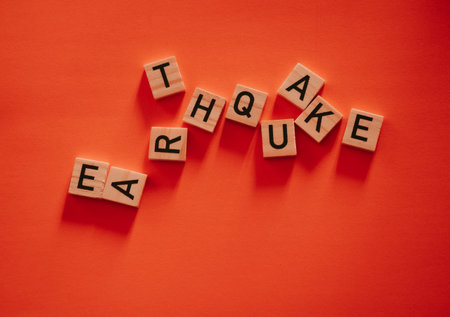 Inscription earthquake from vibration moves on background. Concept of earthquake, destruction and shifts of  earth's crust. Wooden square blocks with letters are laid out on  orange sheet. Slow motionの写真素材