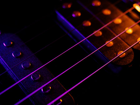 Electric guitar strings close up. Musical instrument details. Concert color contrast lighting. Six-string guitar during performance. Bright colors on dark bsckground. Cinematic light. Copy spaceの写真素材