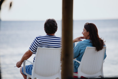A couple of adults sit on chairs at a beach bar on the seashore. Background for a tourist brochure. Fazana, Croatia - circa 2025の写真素材