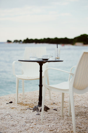 Table with chairs and empty glass and coffee cup on the seashore. Beach bar. Summer evening. Fazana, Croatia - circa 2025の写真素材