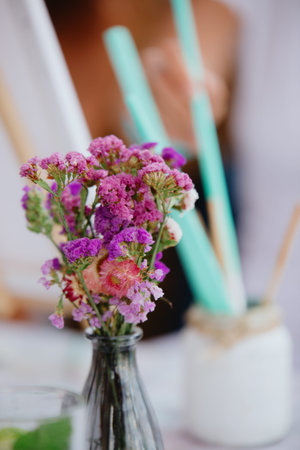 Fresh wild flowers stand in a glass vase on the table. In the background a glass with light green...