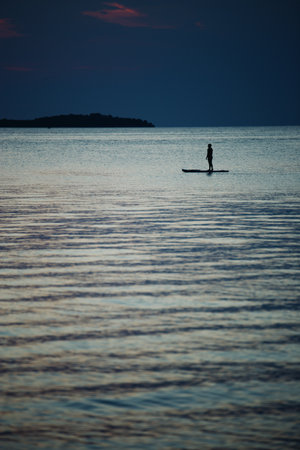Silhouette of a man on a paddleboard in the sea at sunsetの写真素材