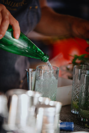 Bartender pouring sparkling water into a glass. Making a Mojito cocktail. Bartender working behind the bar.の写真素材
