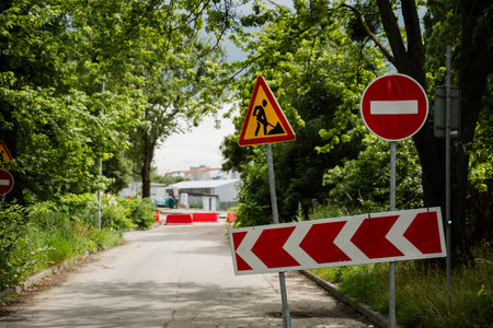 Construction area features warning signs and barriers, with vibrant greenery lining the road, indicating ongoing work and restricted accessの写真素材
